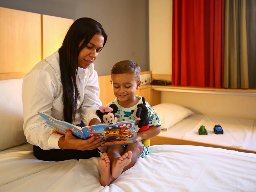 Una mujer y un niño sentados en una cama, leyendo un libro juntos.