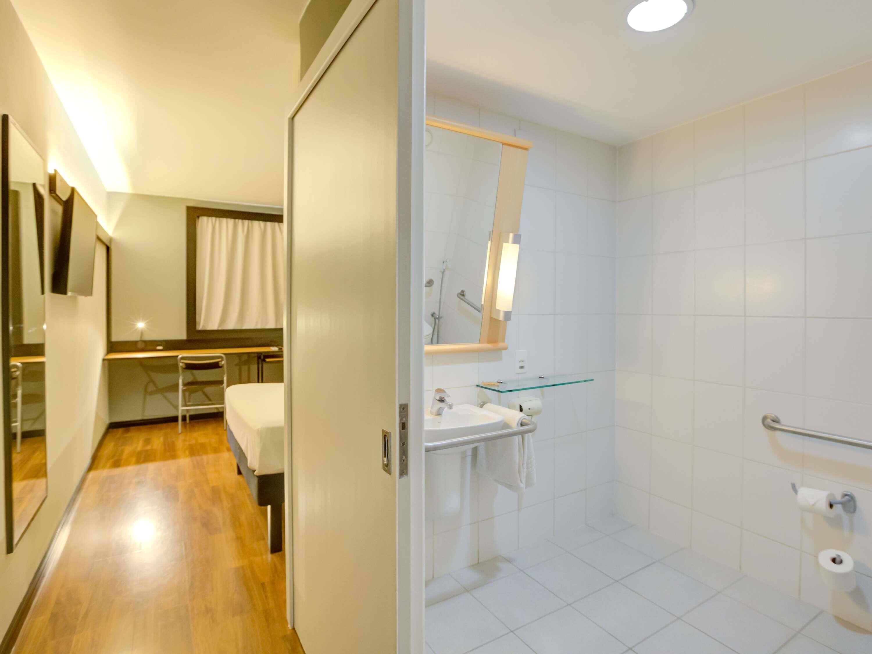 Casa de banho de hotel com lavatório, espelho e chuveiro.