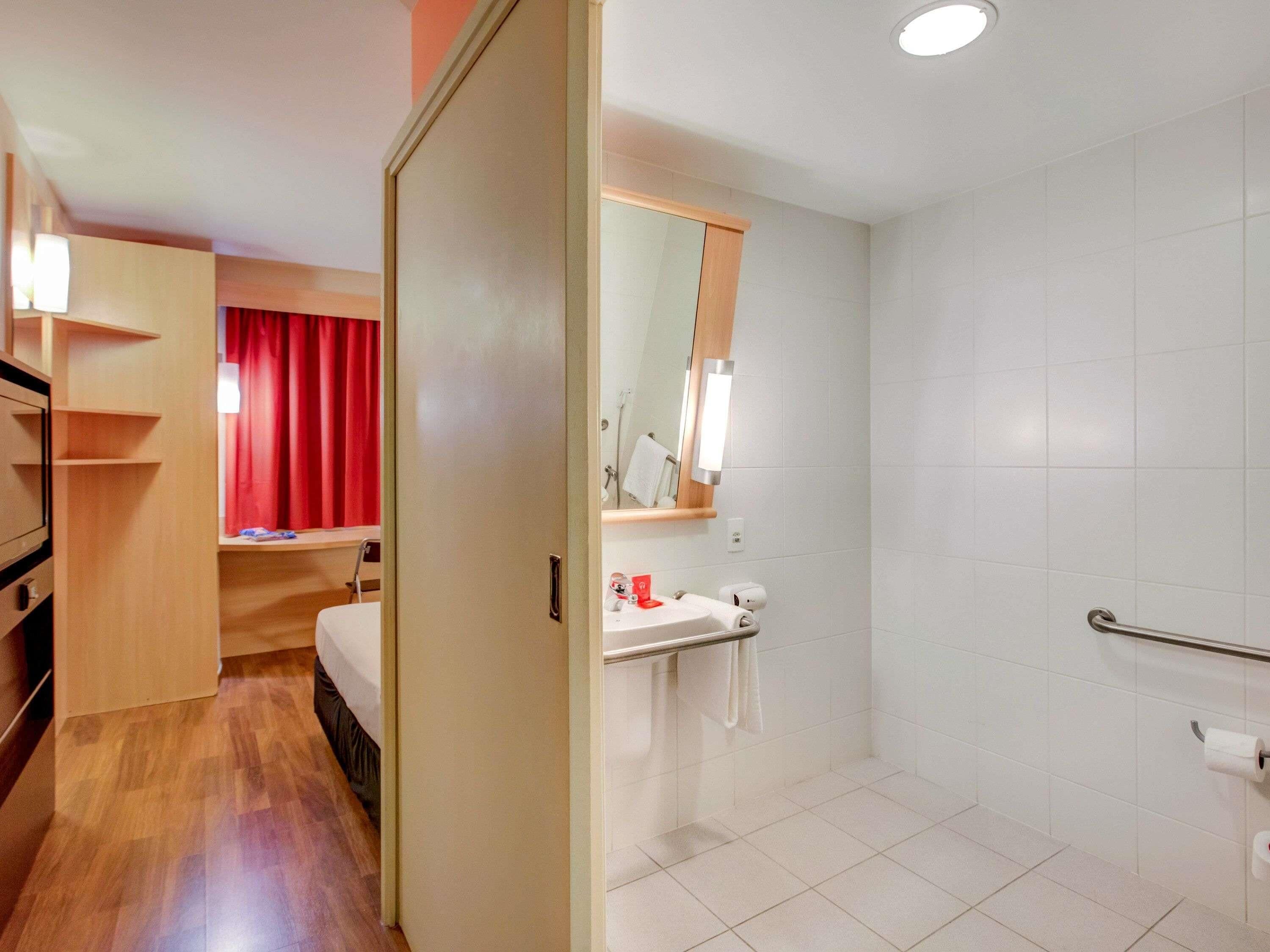 A hotel room with a bed, a bathroom with a shower, a sink, and a mirror.