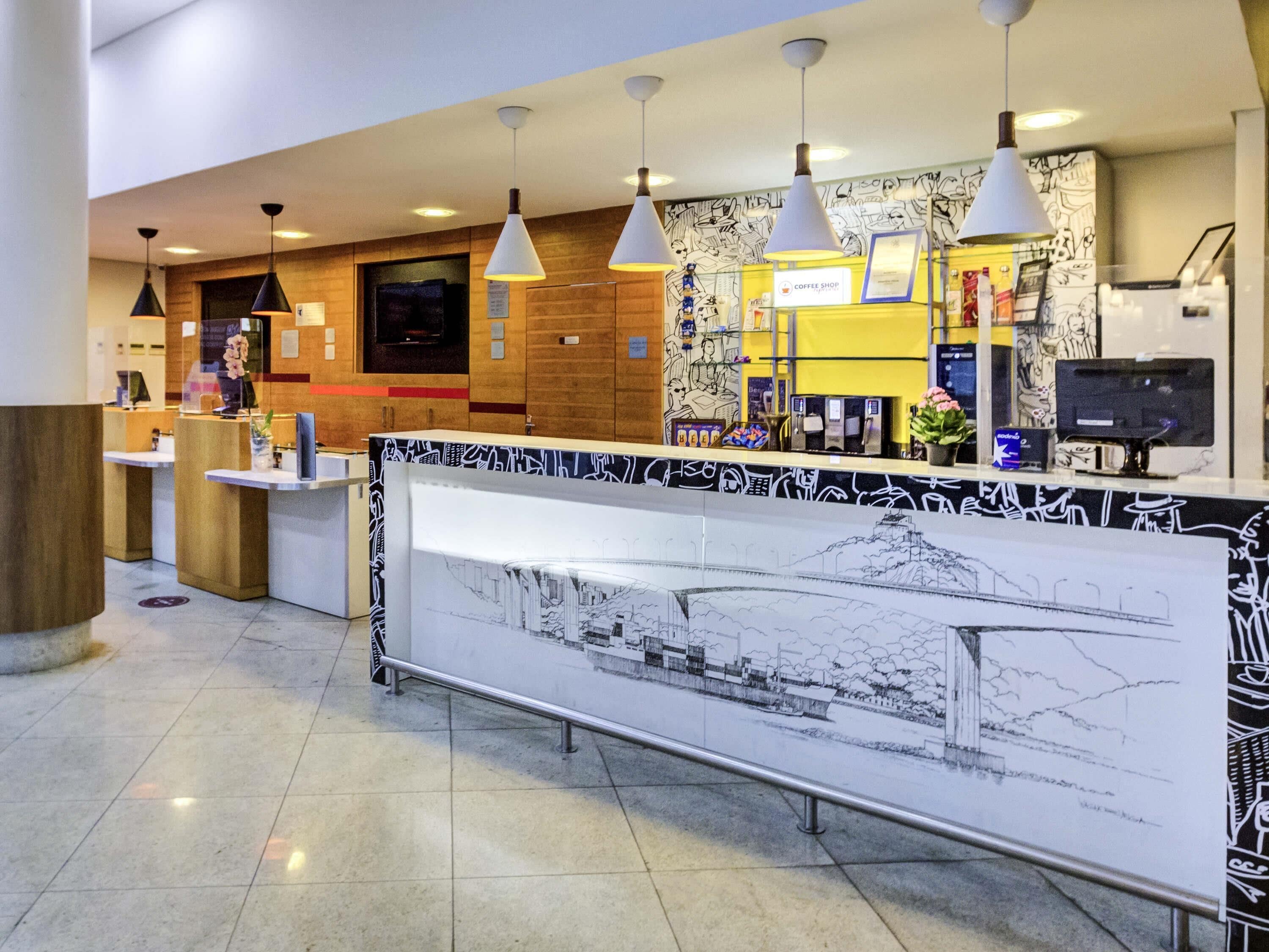 A coffee shop with a counter, hanging pendant lights, and a mural on the wall.