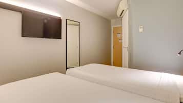 Habitación de hotel con dos camas individuales, un televisor de pantalla plana montado en la pared, una puerta y un equipo de aire acondicionado.