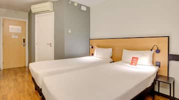 Quarto de hotel com duas camas, piso de madeira, parede cinza e aparelho de ar condicionado.