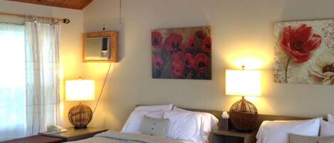 Quarto de hotel com duas camas, vigas de madeira no teto, ventoinha no teto, janela com cortinas e ar-condicionado fixado na parede.