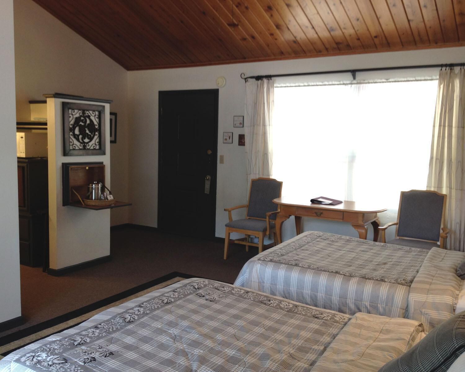 Et hotelværelse med to senge, trælofter, et lille bord med stole, et køleskab og en hylde med elkedel.