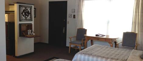 A hotel room with two beds, a wooden ceiling, a small table with chairs, a refrigerator, and a shelf with a kettle.
