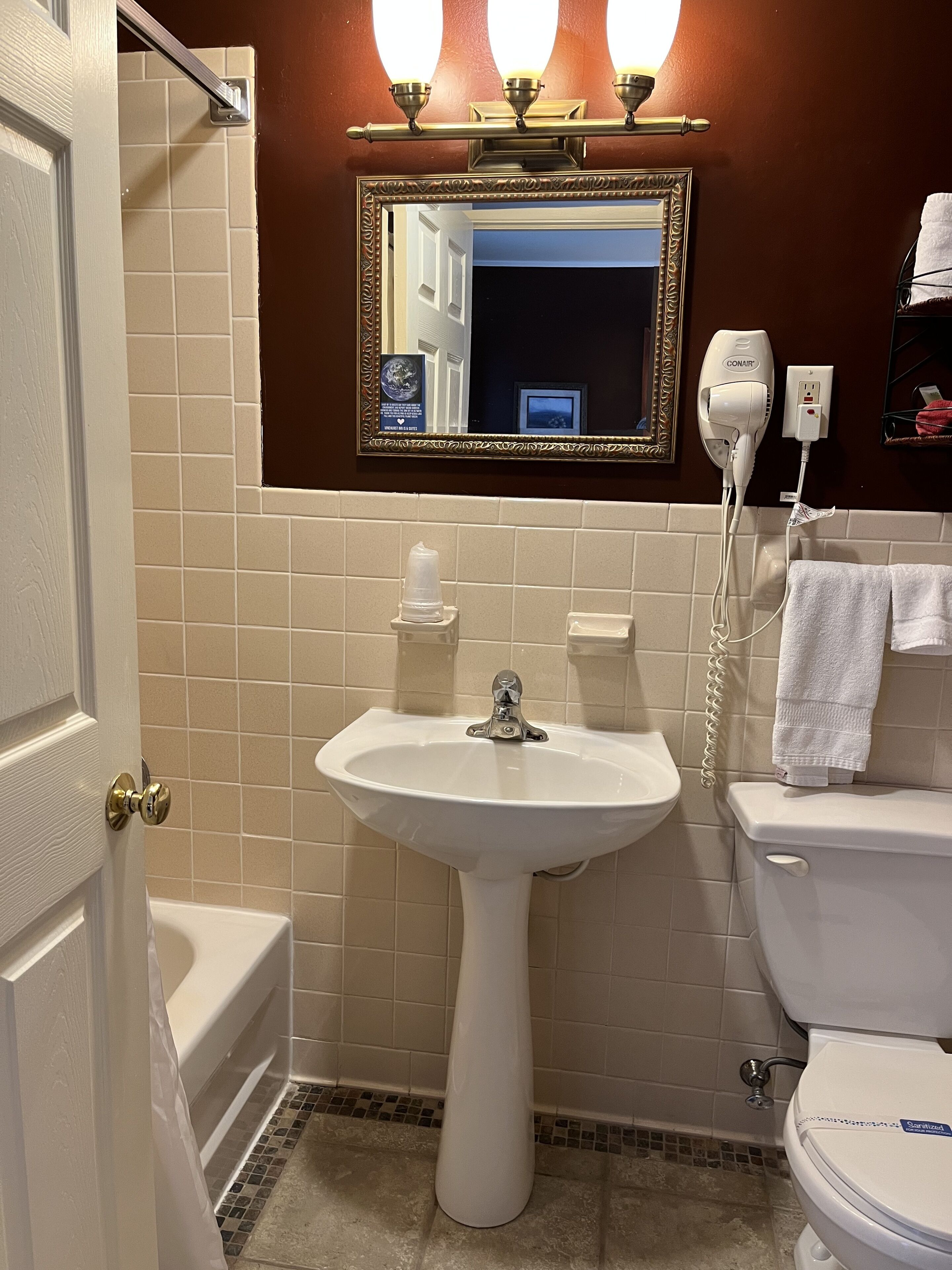 Et badeværelse med et pedalvask, toilet, badekar og et spejl over et toiletbord.