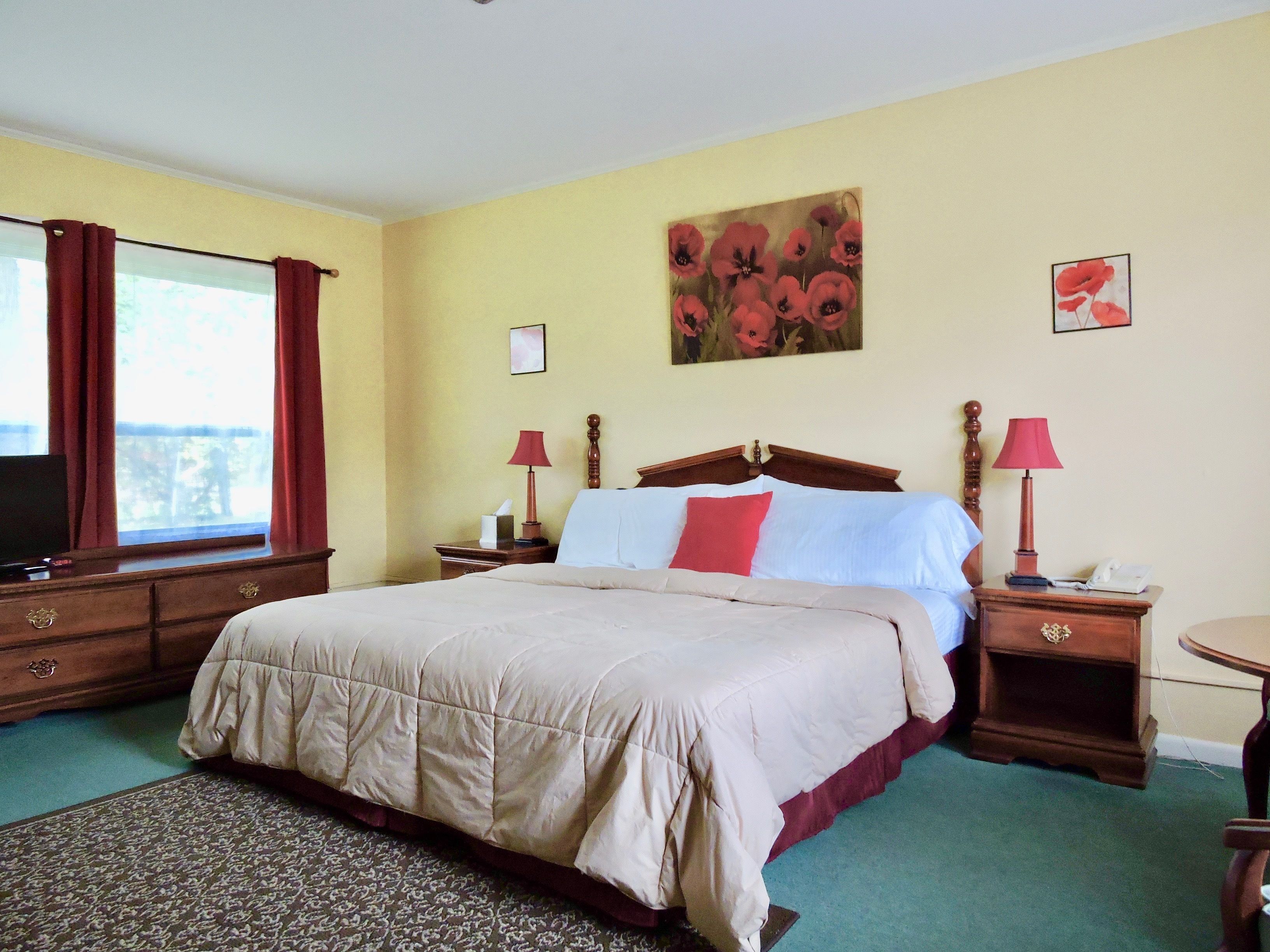 Quarto de hotel com uma cama grande, duas mesas de cabeceira com luminárias, uma TV e uma janela com cortinas.