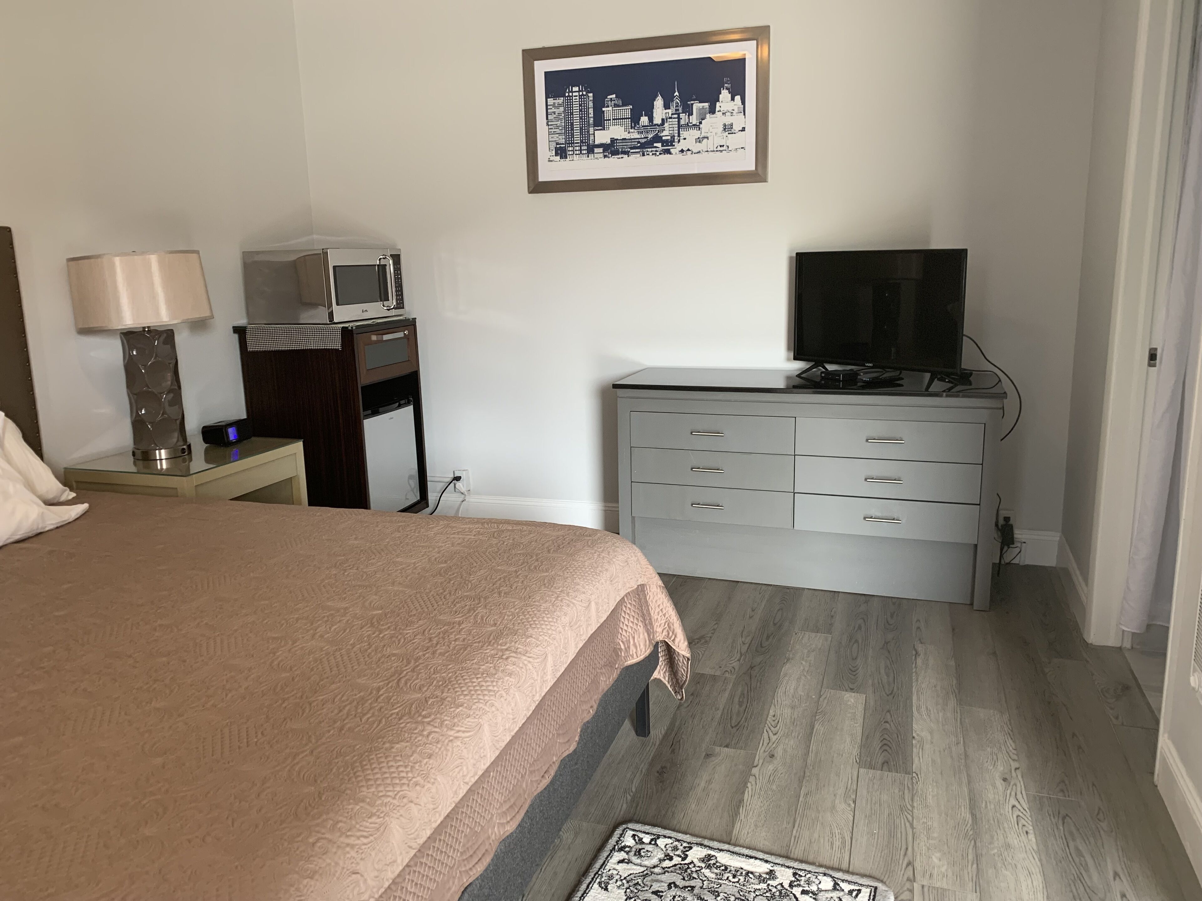 A hotel room with a bed, a desk with a lamp, a television, and a dresser.