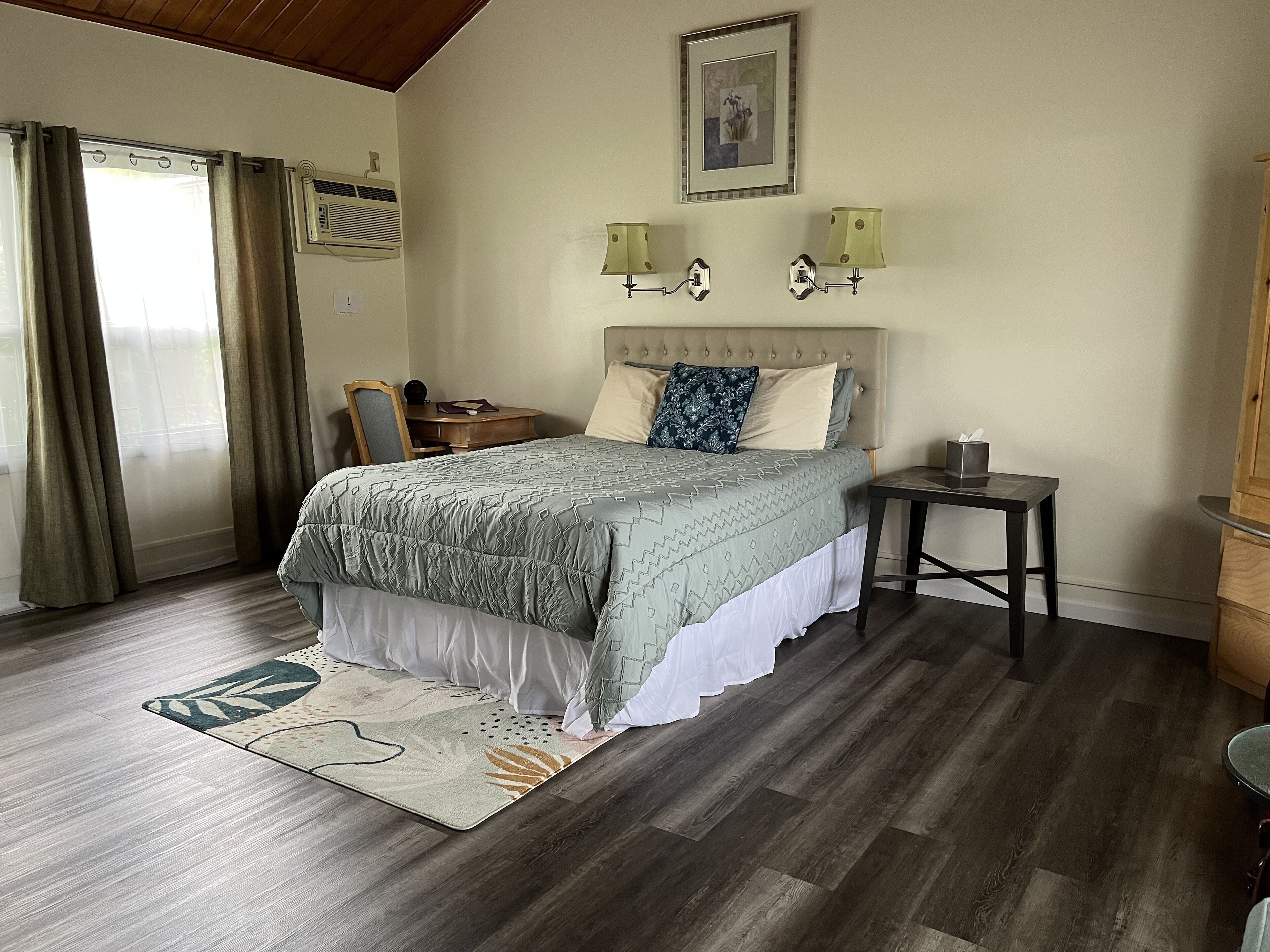 A bedroom with a bed, bedside table, lamp, and a desk with a chair.