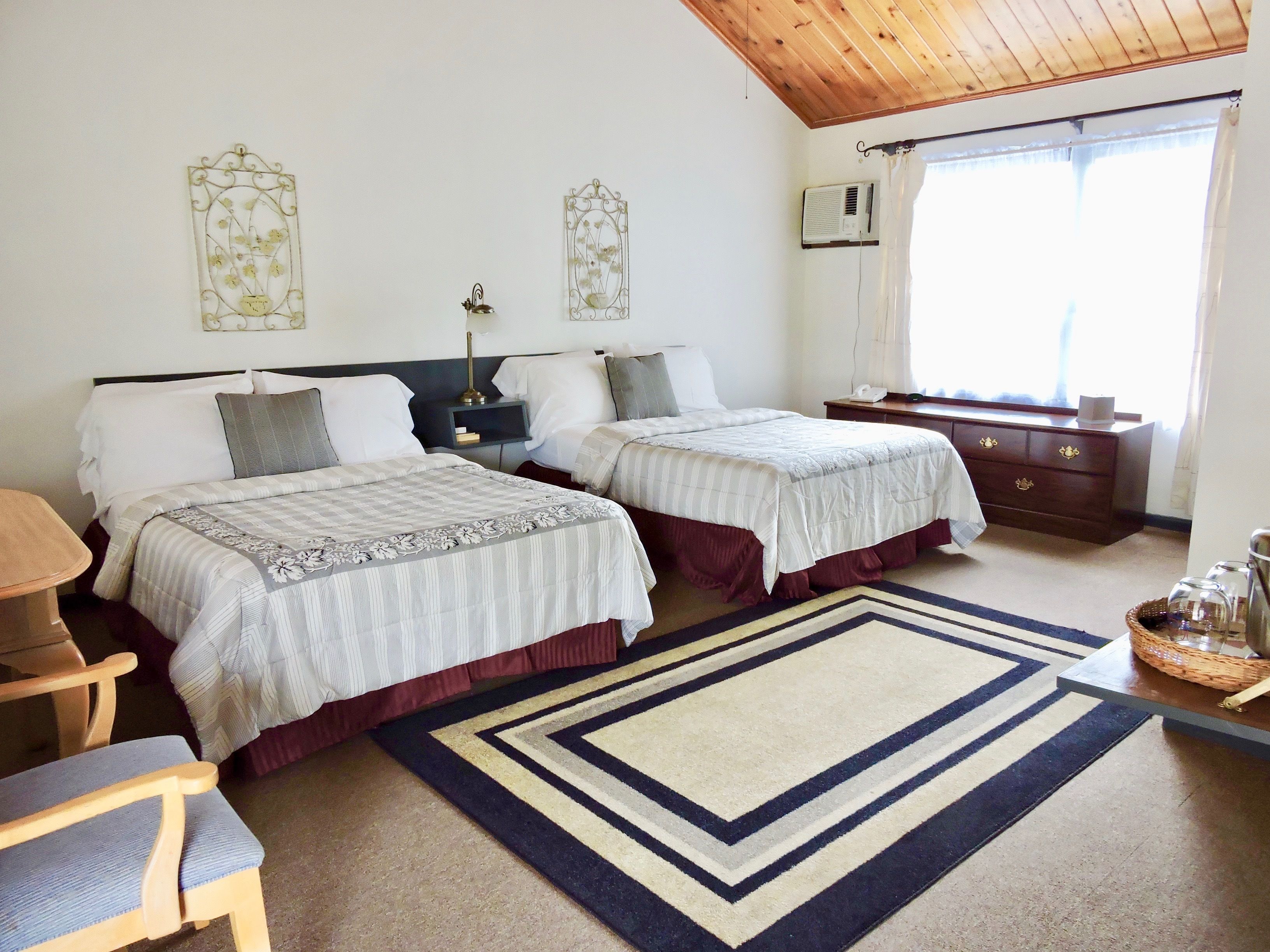 Une chambre avec un grand lit, deux lits simples, une table de chevet, une commode et une fenêtre avec des rideaux.