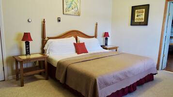 A neatly made bed with a wooden headboard, two bedside tables with lamps, a red throw pillow, and a framed picture on the wall.