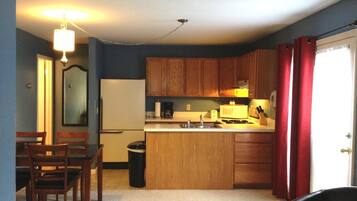 A compact kitchen with wooden cabinets, a refrigerator, a stove, and a sink. There is a dining area with chairs and a table.