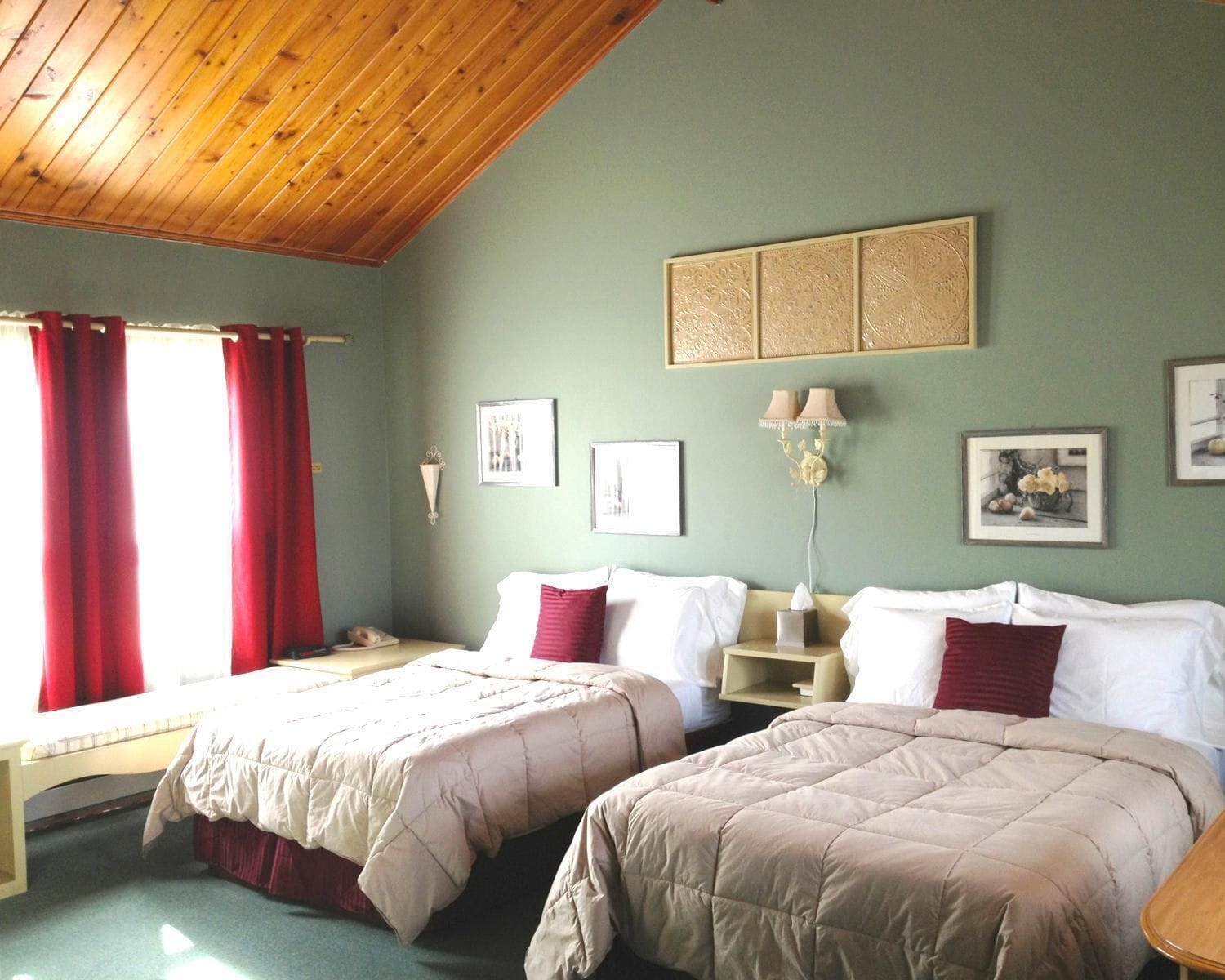 Una habitación con dos camas, techo de madera y pared verde decorada con cuadros.