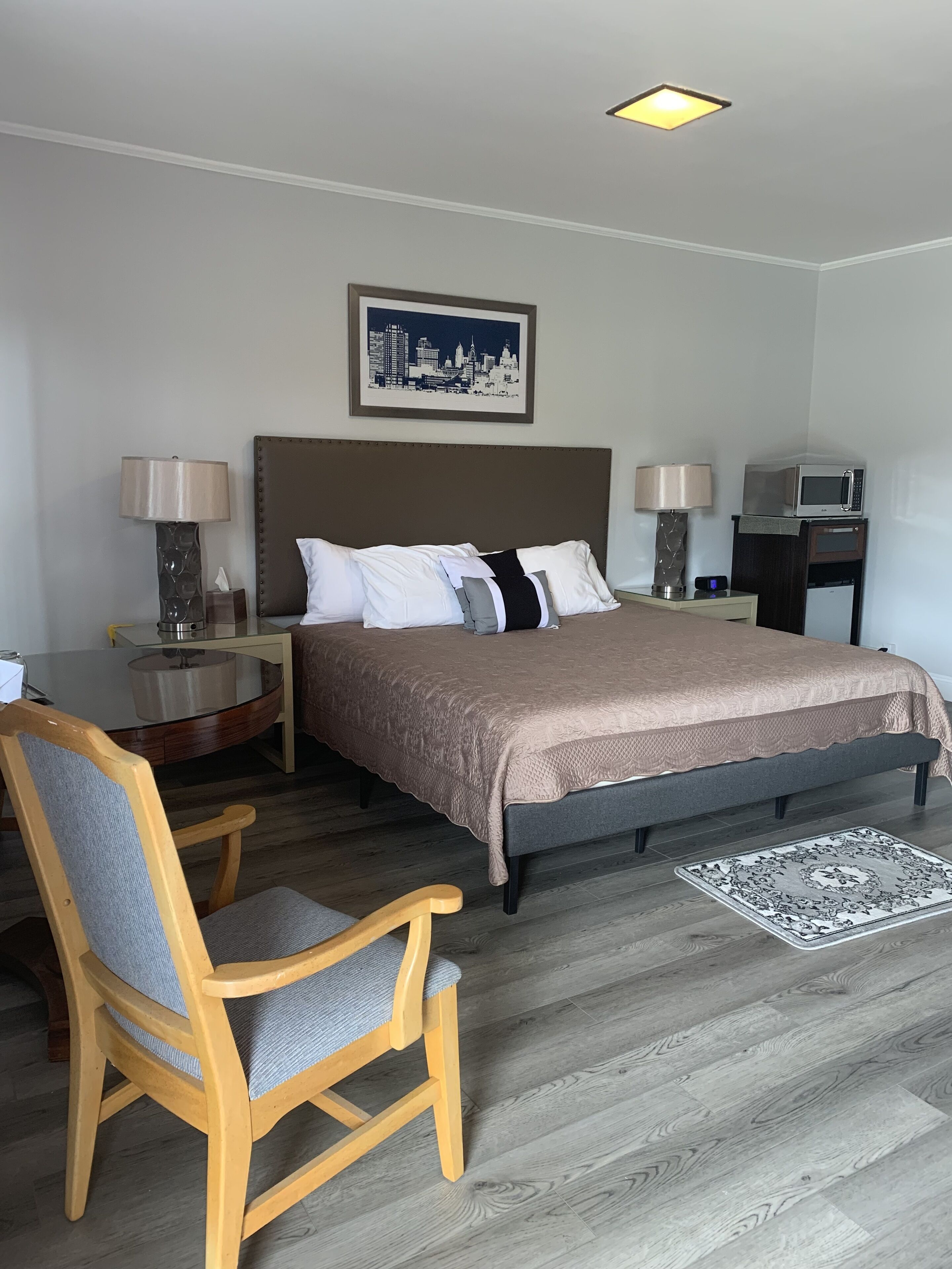 Quarto de hotel com cama, duas mesas de cabeceira, escrivaninha, cadeira, abajur, quadro na parede e micro-ondas.
