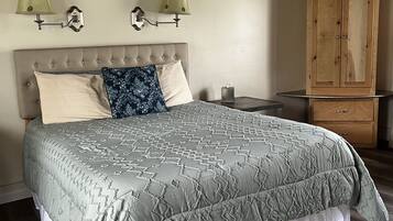 A bedroom with a large bed, two wall-mounted lamps, a wooden cabinet, and a framed picture on the wall.