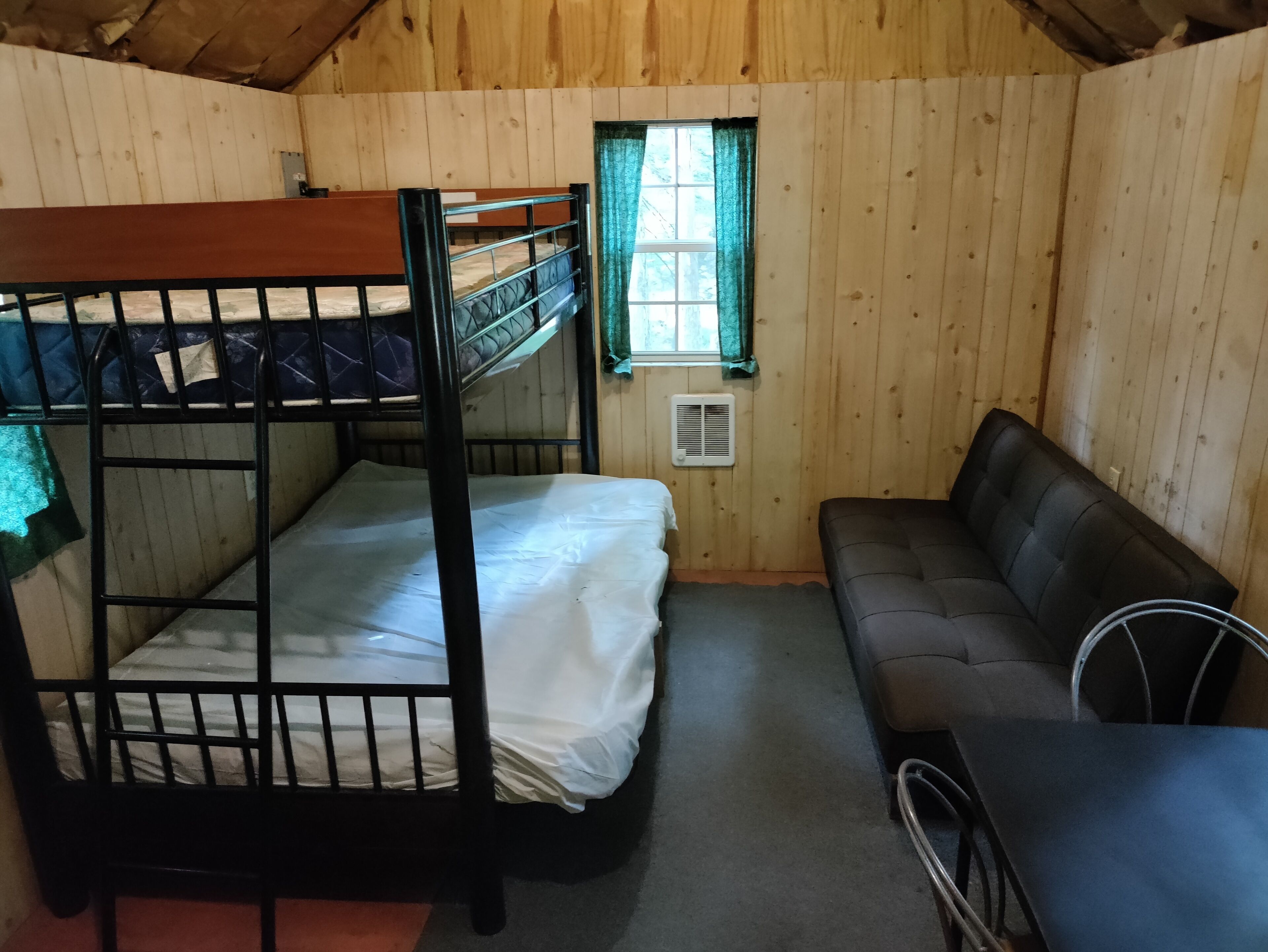 Ein Stockbett mit einer Matratze, eine Schlafcouch und ein kleiner Tisch in einem Holzraum.