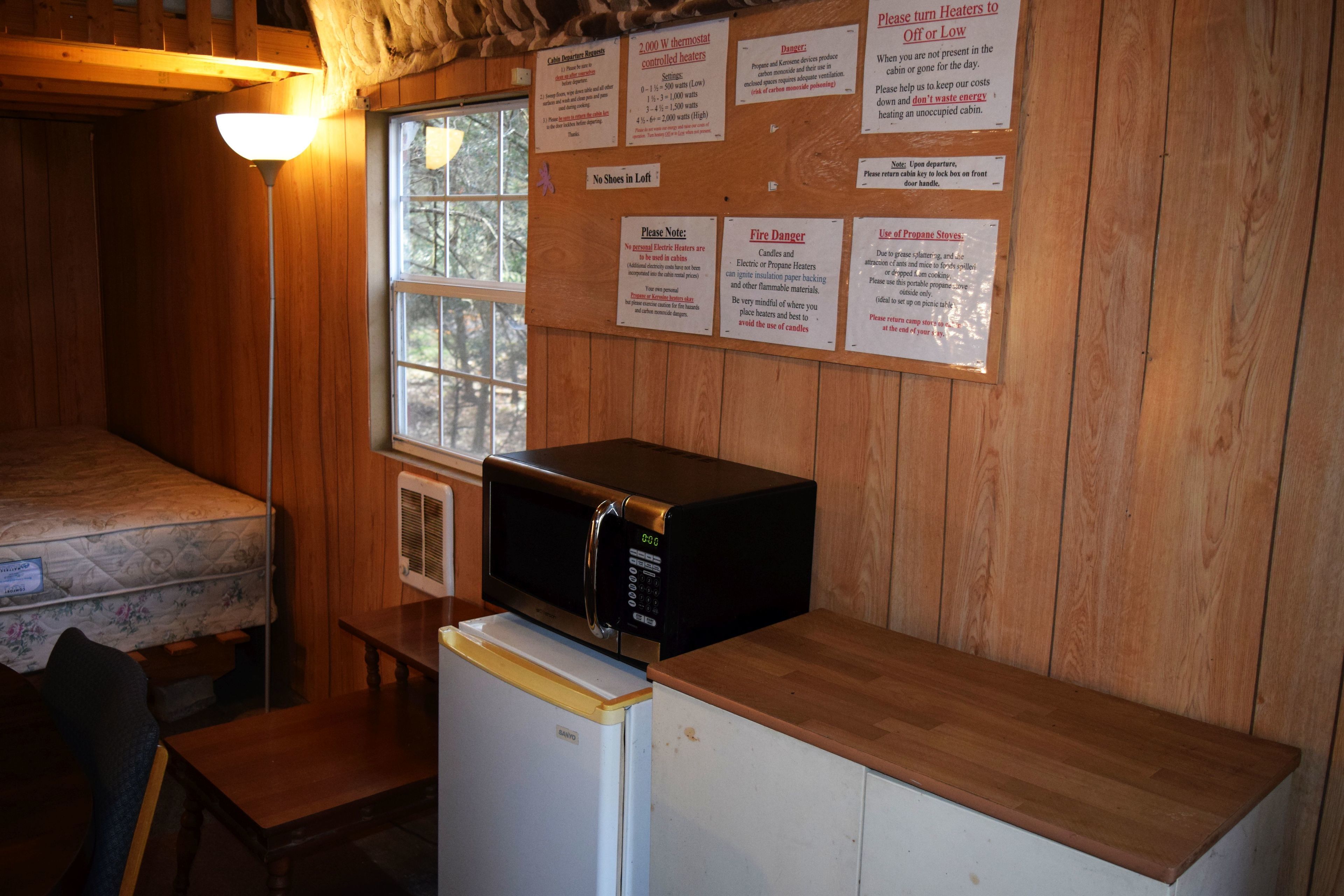 A compact kitchen area with a microwave on a wooden counter, a refrigerator, and a window with a view of trees.