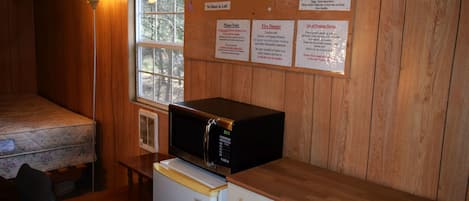 A compact kitchen area with a microwave on a wooden counter, a refrigerator, and a window with a view of trees.