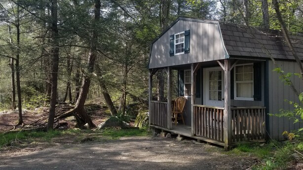 Eine kleine Holzhütte mit Veranda, umgeben von einem Wald.