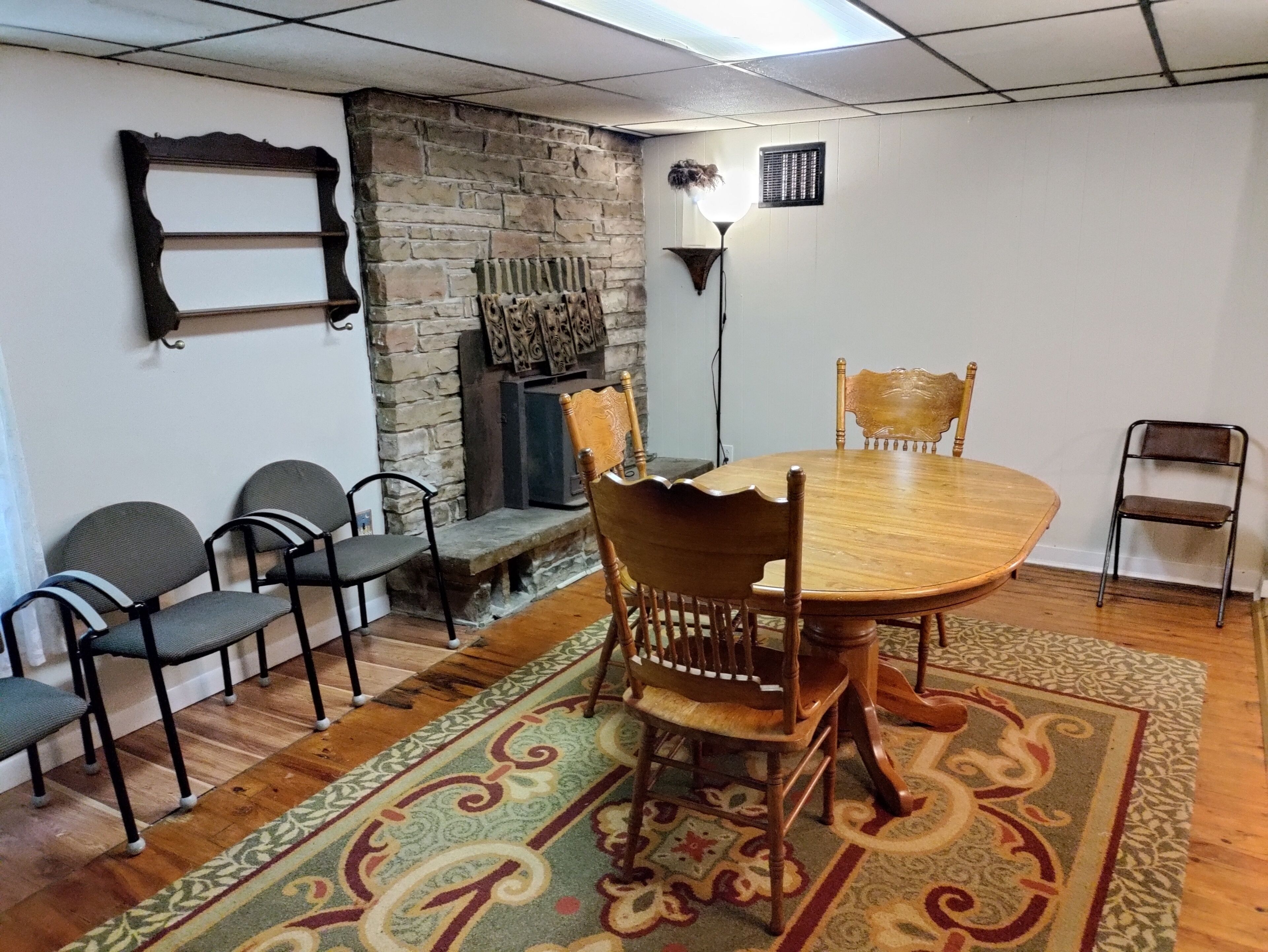 Un coin repas comprenant une table ronde en bois, quatre chaises, un tapis à motifs, une cheminée en pierre et un luminaire fixé au mur.