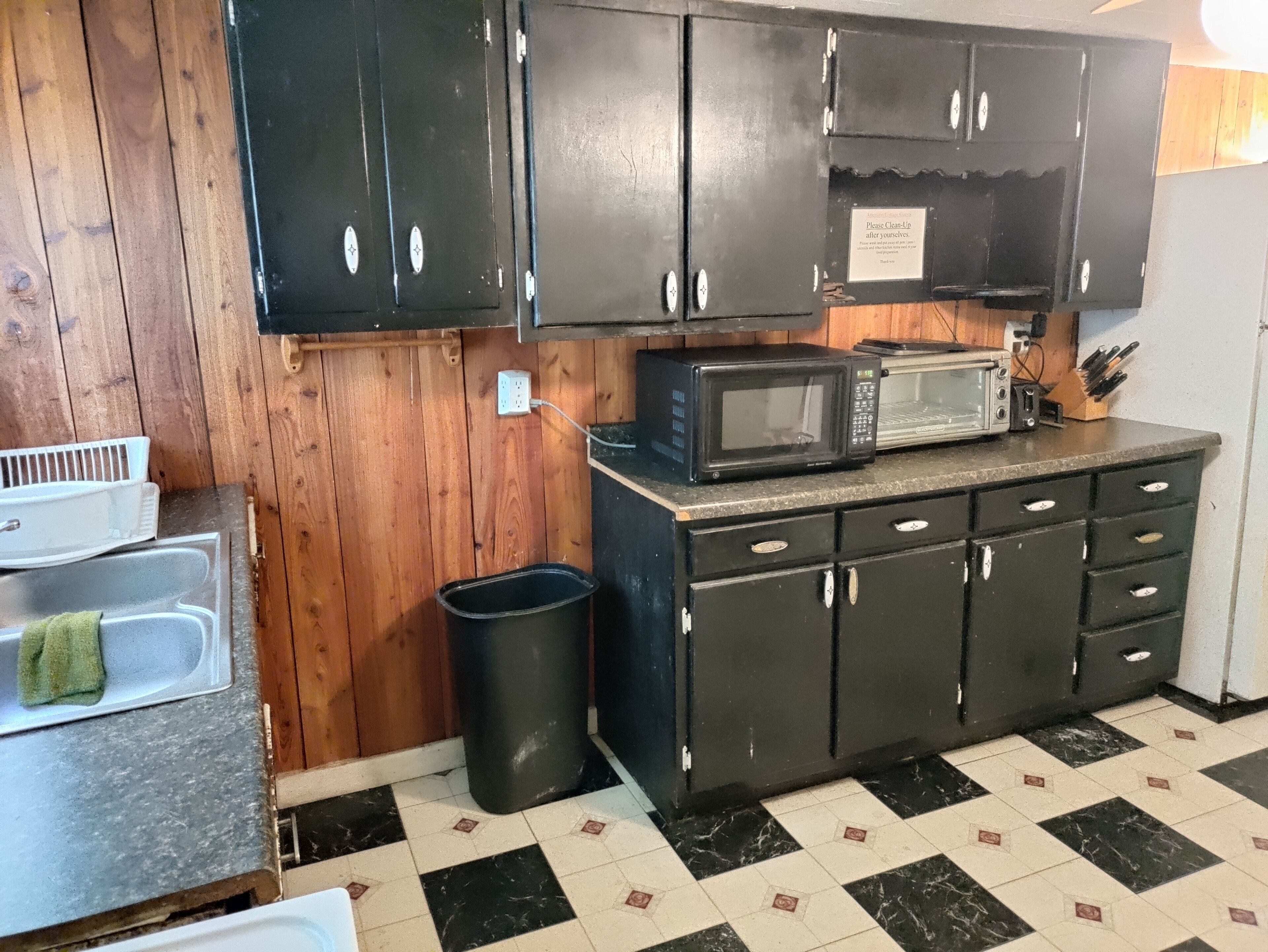 A kitchen with wooden cabinets, a microwave, a toaster, and a trash can.