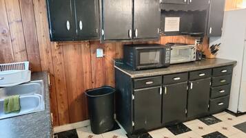 A kitchen with wooden cabinets, a microwave, a toaster, and a trash can.