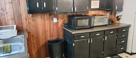 A kitchen with wooden cabinets, a microwave, a toaster, and a trash can.