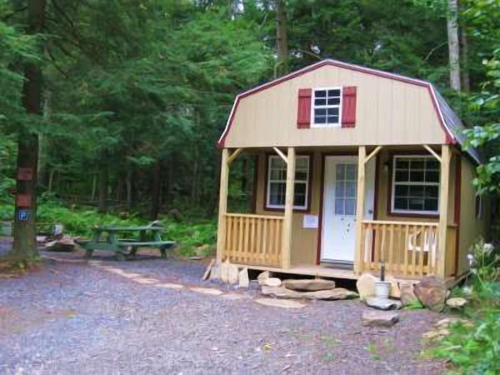 A small wooden cabin with a porch, surrounded by trees.