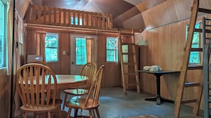 Ein gemütliches Blockhaus mit Holzwänden, einer erhöhten Schlafkoje, einem Esstisch mit Stühlen und einer Leiter.