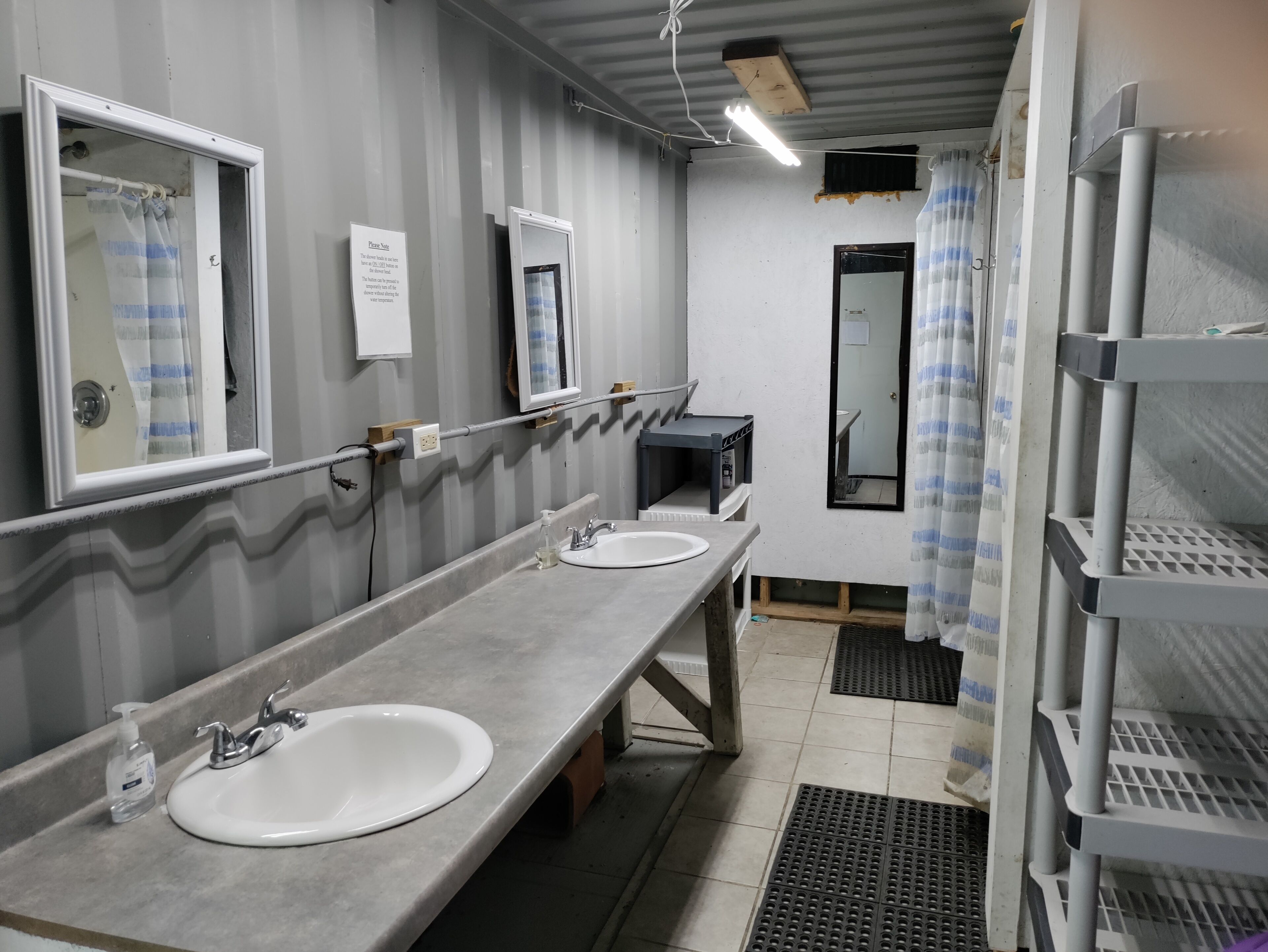 Baño público con dos lavamanos, espejos y zona de ducha.