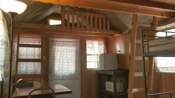 Interior rústico de una cabaña con paredes de madera, un área de dormir en un entrepiso, una mesa de comedor y un televisor.