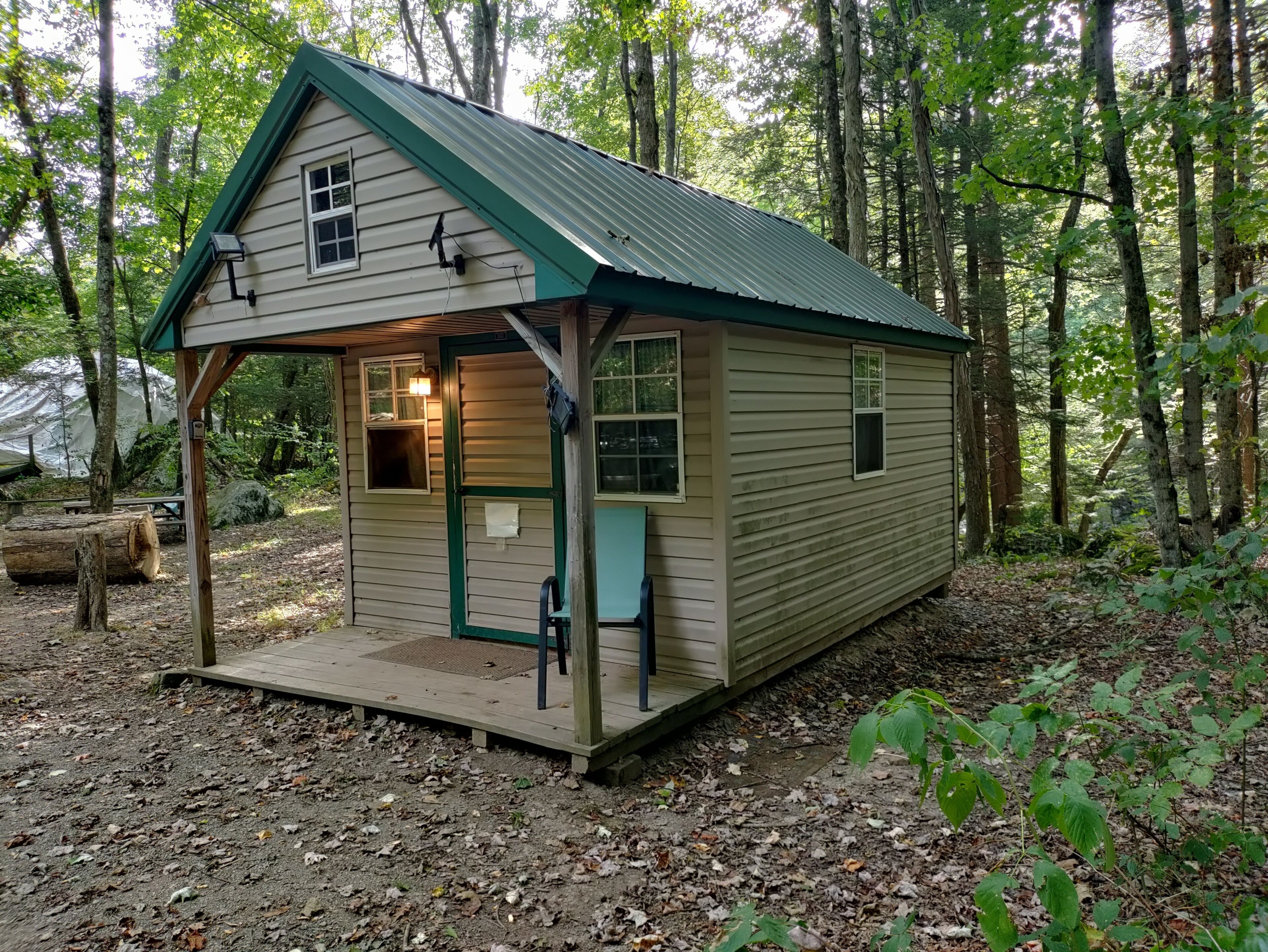 A small wooden cabin with a green roof, a porch, and a single window.