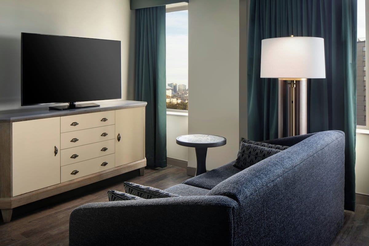 A modern living room with a flat-screen TV, a sofa, a small round table, and a lamp.