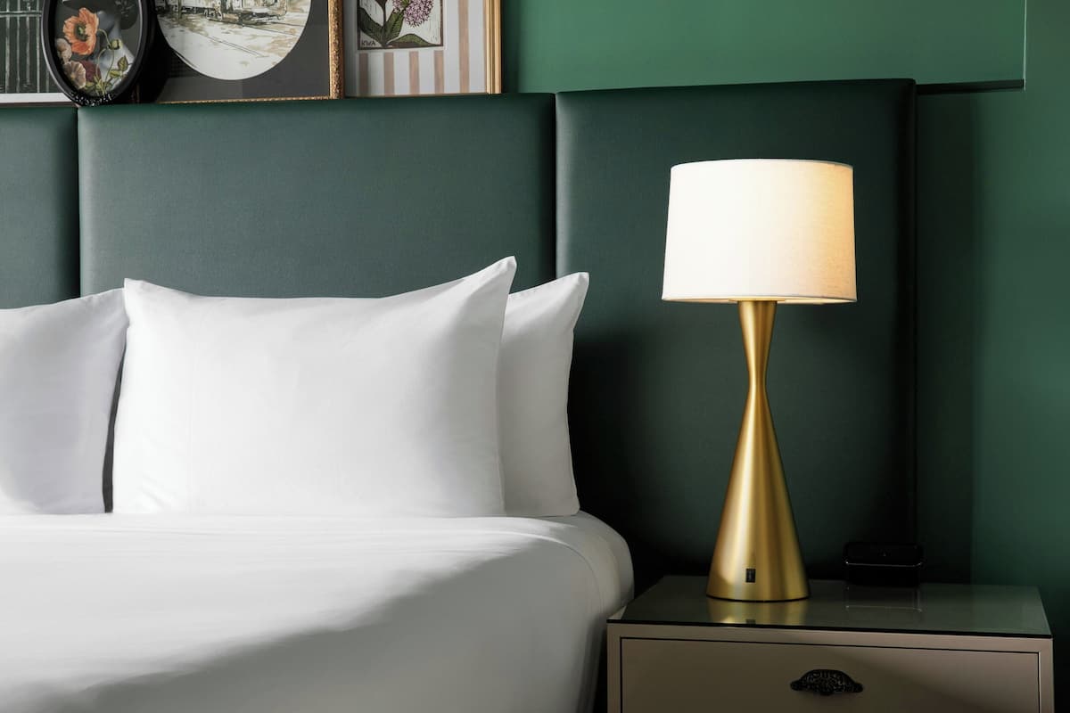 A neatly made bed with white linens and a gold lamp on a bedside table.