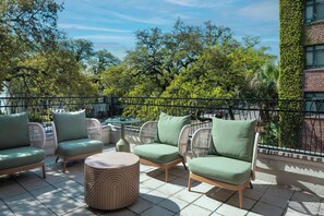 Eine Terrasse mit Korbmöbeln, einem runden Tisch und Blick auf Bäume und ein Gebäude.