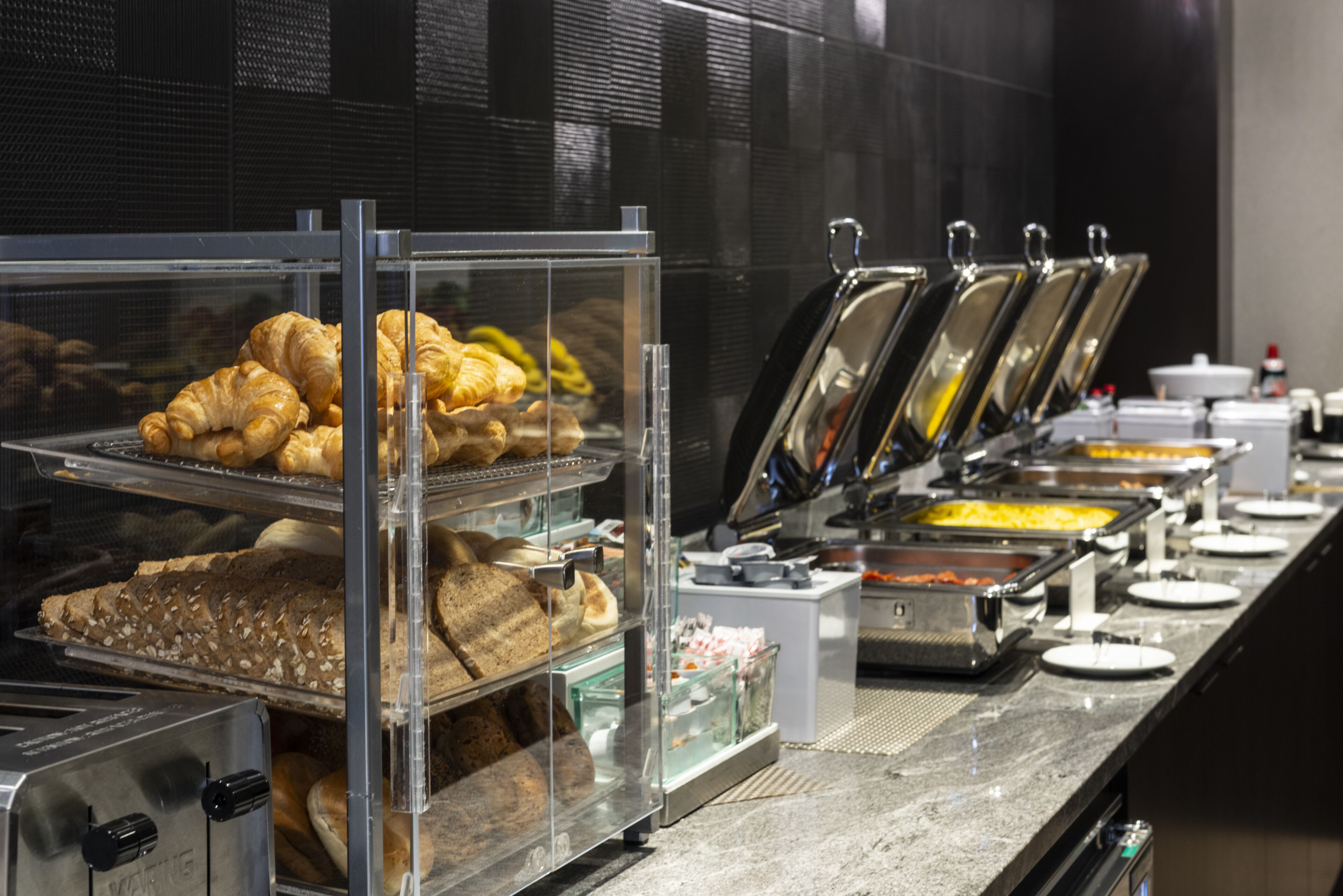 Un buffet con diversi cibi, tra cui pasticceria e piatti caldi, esposti in contenitori trasparenti.