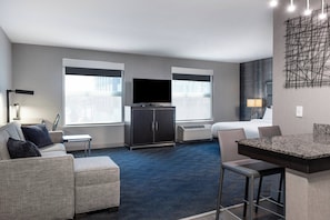 A modern hotel room with a large flat-screen TV, a sofa, a dining area, and a large window providing a city view. - Residence Inn Boston Logan Airport/Chelsea (Chelsea)