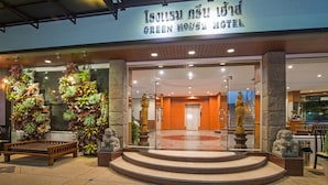 El exterior del Hotel Green House, con una entrada amplia, una estatua de león de piedra y un cartel en idioma extranjero.