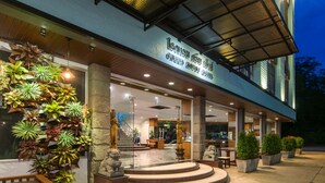 Entrada de hotel con una escalera que lleva al vestíbulo, plantas en macetas y un cartel sobre la entrada.