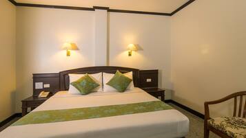Una habitación de hotel con una cama grande, dos mesitas de noche con lámparas, una silla y un teléfono en una de las mesitas.