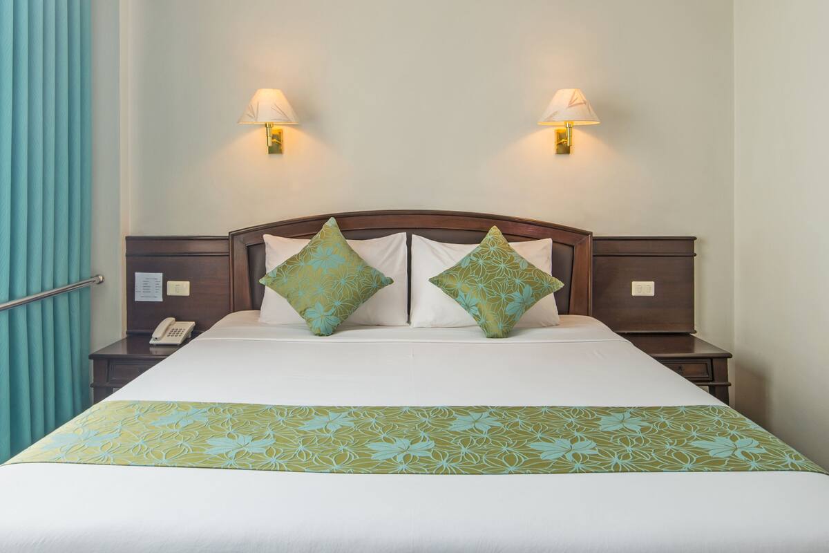 Une chambre d’hôtel avec un lit, deux tables de chevet, un téléphone et un rideau bleu.