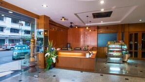 Zona de recepción de hotel con un mostrador de madera, una caja registradora y un refrigerador lleno de bebidas.