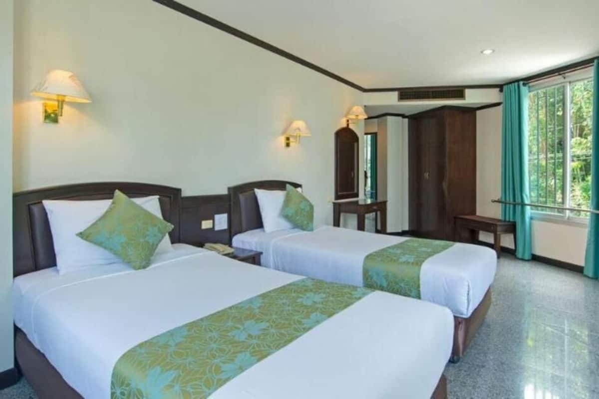 Une chambre d’hôtel avec deux lits, un miroir, un bureau et une fenêtre avec des rideaux.