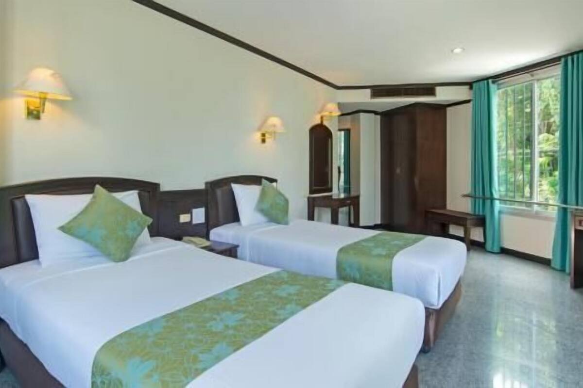 Une chambre d’hôtel avec deux lits, un bureau, un miroir et une fenêtre avec des rideaux.