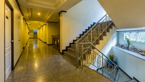 Un pasillo de hotel con piso de granito pulido, una escalera con barandales de metal y una ventana con vistas al exterior.