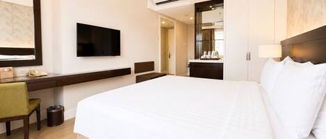 A hotel room with a bed, a desk, a chair, a TV, a mirror, and a bathroom.