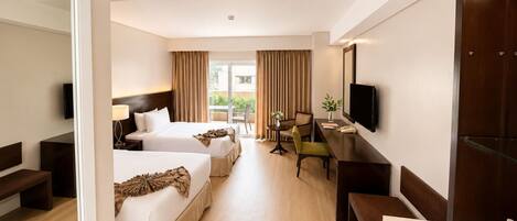 A hotel room with two beds, a desk, a chair, a TV, and a view of the outdoors.