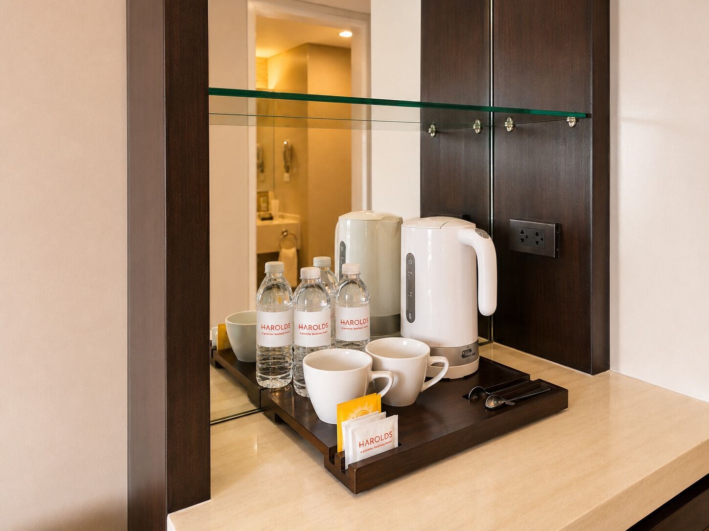 A hotel room with a glass partition, a coffee maker, cups, and bottles on a tray.