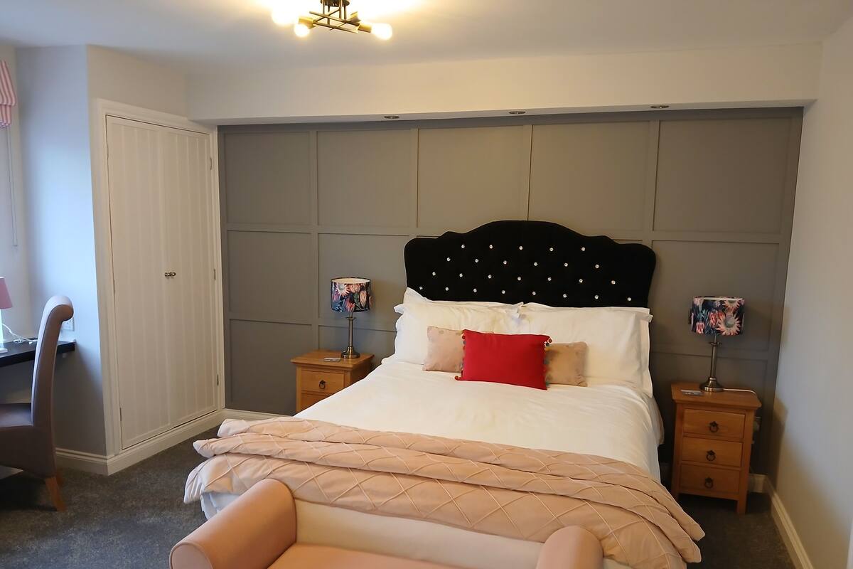 Un dormitorio con cama, mesitas de noche, una silla y un armario.