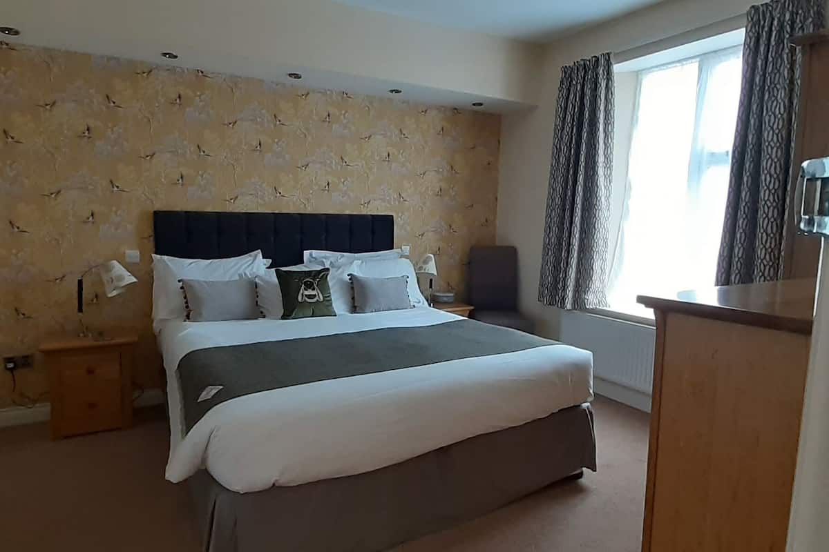 Una habitación de hotel con una cama grande, una mesita de noche, una lámpara, un aparador y una ventana con cortinas.